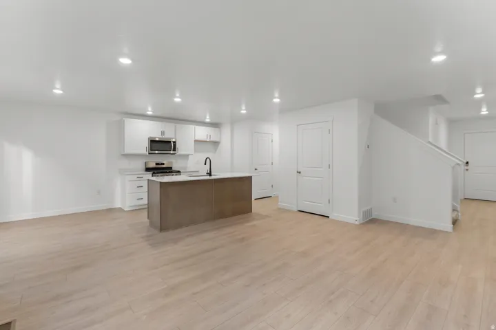 Modern kitchen featuring white cabinetry, stainless steel appliances, a center island with a black faucet, light wood-finish flooring, and recessed lighting