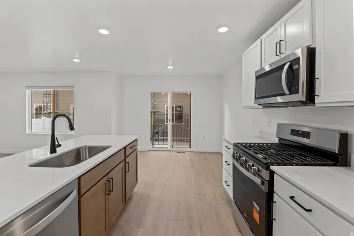 Modern kitchen featuring an expansive center island with an undermount sink, stainless steel appliances, white cabinetry, and wood-finish flooring