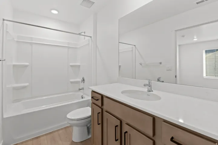Bathroom featuring a shower/tub combination with integrated shelving, a single vanity with a white countertop and undermount sink, wood-finish flooring, and a large wall-mounted mirror