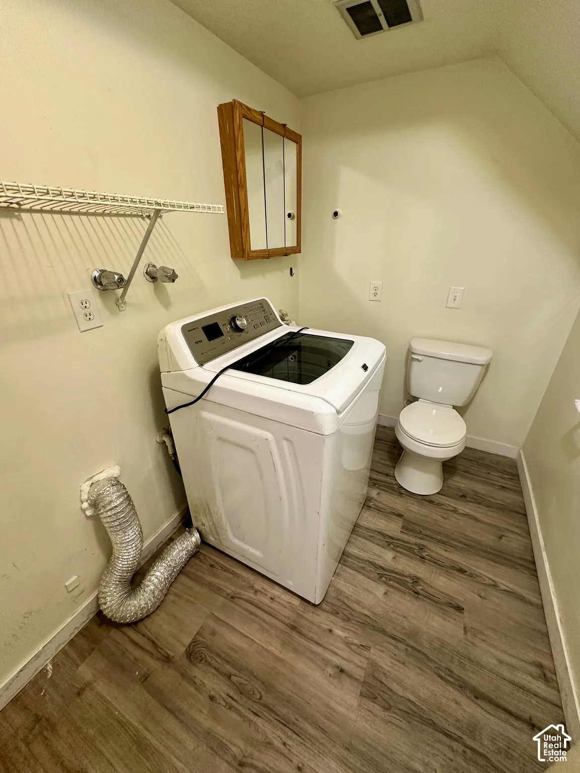 Dedicated laundry area featuring wood-finish flooring, a wall-mounted storage cabinet, and an overhead wire shelf
