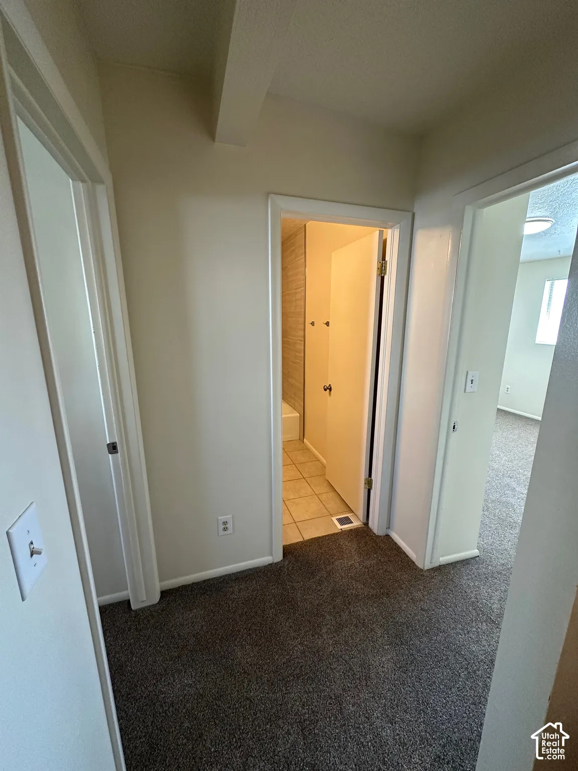 Hallway featuring dark gray carpet flooring, light neutral wall paint, and white trim
