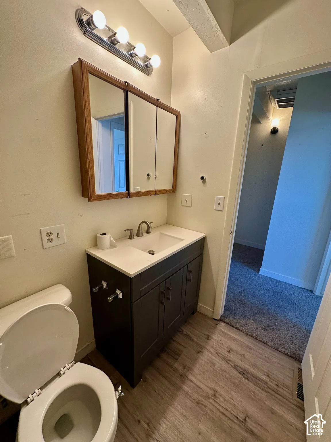 Bathroom featuring a dark wood-finish vanity with a white countertop and integrated sink, a chrome faucet, and a tri-fold medicine cabinet with a wood-finish frame