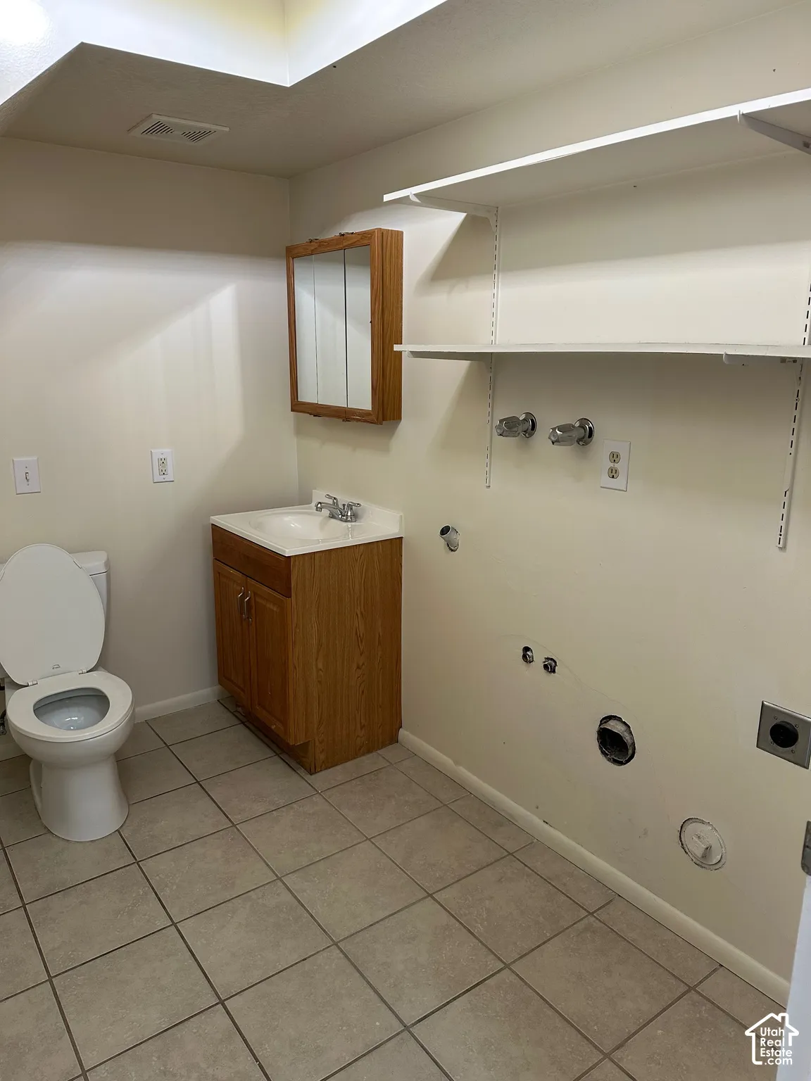 Utility room featuring a built-in wood-finish vanity with an integrated sink, wall-mounted medicine cabinet, white shelving, and tile flooring