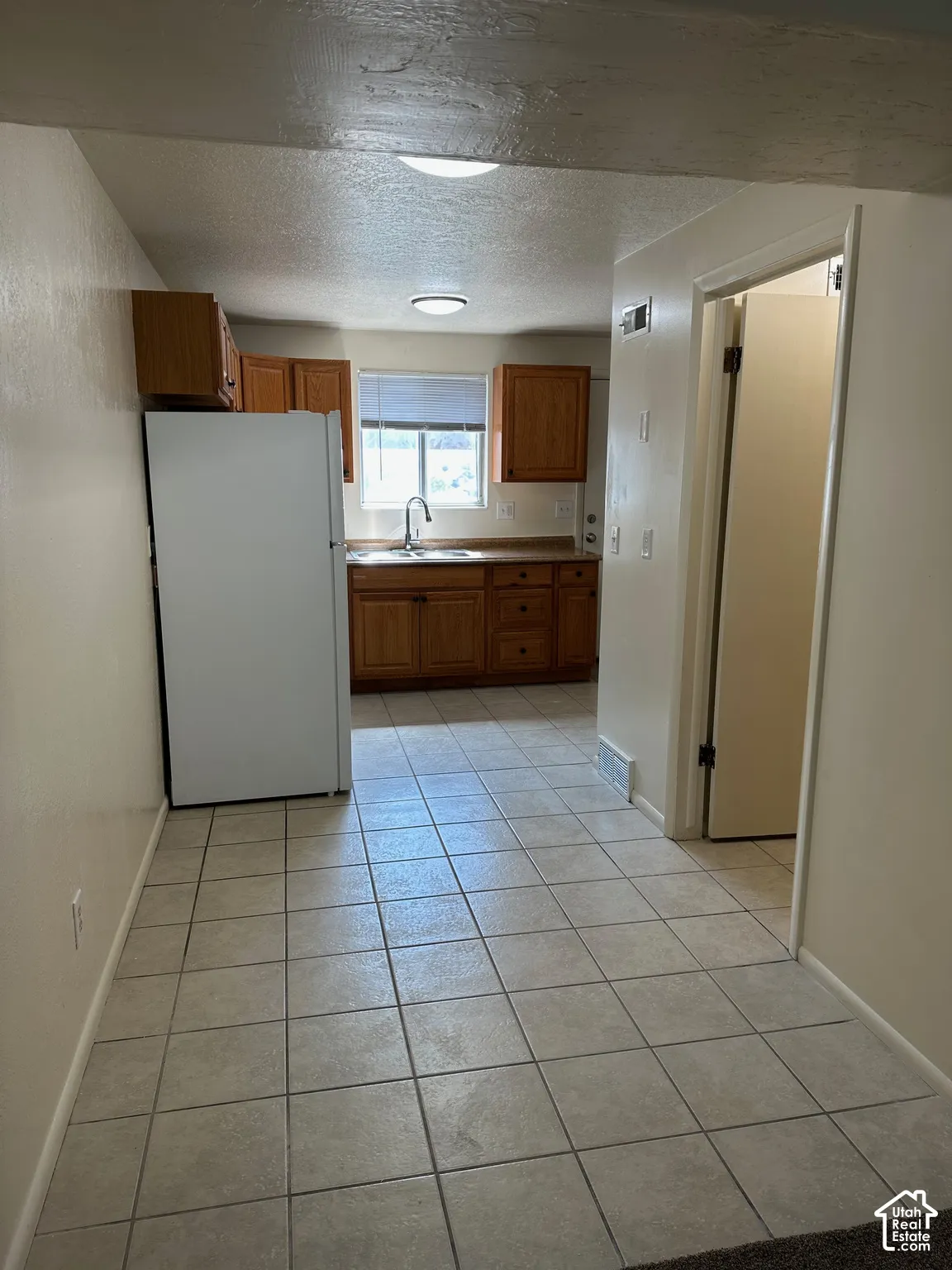 Kitchen featuring tile flooring, wood cabinetry, a stainless steel sink, and a window with blinds