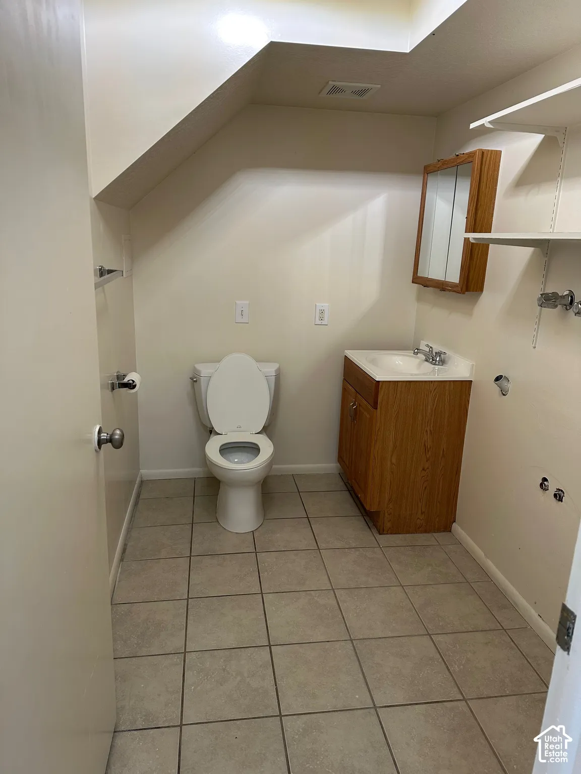 Full bathroom featuring a white toilet, wood-finish vanity with an integrated sink, and a mirrored medicine cabinet