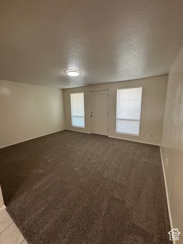 Spacious room featuring textured carpeting, neutral wall finishes, and a white entry door