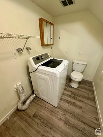 Dedicated laundry area featuring wood-finish flooring, a wall-mounted storage cabinet, and an overhead wire shelf