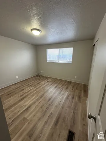 Spacious room featuring wood-finish flooring, neutral-toned walls, a single window with blinds, and a flush-mount ceiling light fixture