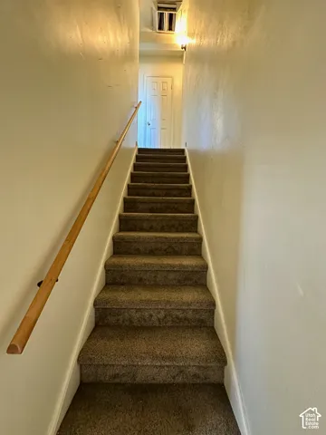 Carpeted staircase with a wood handrail leading to a paneled door
