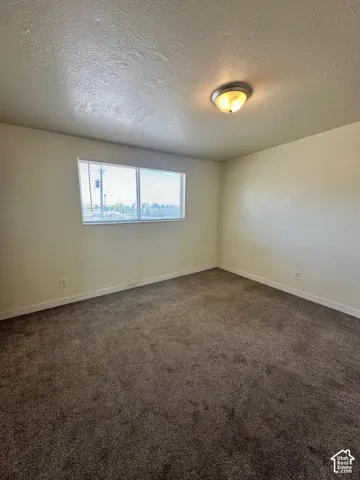 Spacious room featuring neutral-toned carpet, light-colored walls, and a large window with blinds