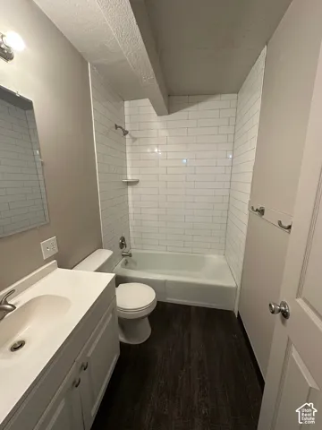 Full bathroom featuring a white vanity with integrated sink, white subway tile shower surround, and dark wood-finish flooring