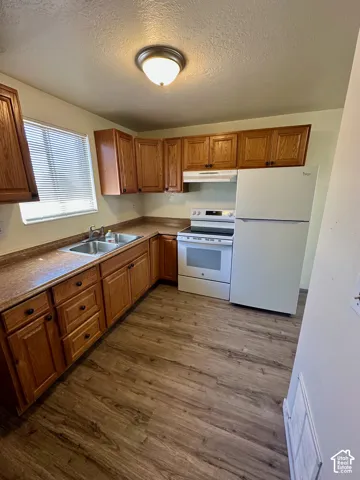 Kitchen featuring wood-finish cabinetry, white appliances, dual basin sink, and wood-finish flooring