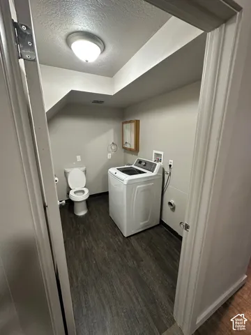 Practical utility room featuring wood-finish flooring, a toilet, a laundry hookup, and a wall-mounted medicine cabinet