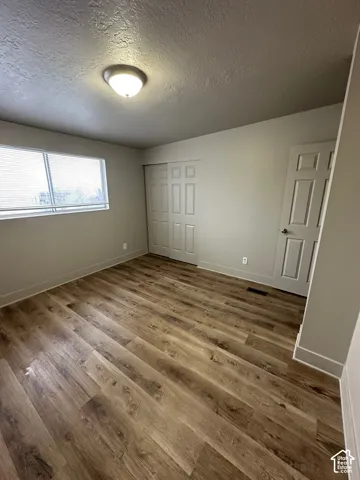 Spacious room featuring wood-finish flooring, a contemporary ceiling light fixture, a window with blinds, and white bi-fold closet doors