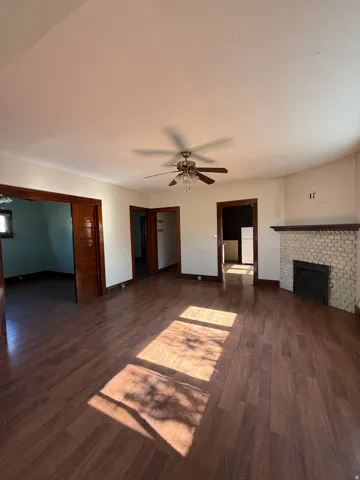 Spacious living area featuring wood-finish flooring, a ceiling fan, and a painted brick fireplace with a dark mantel