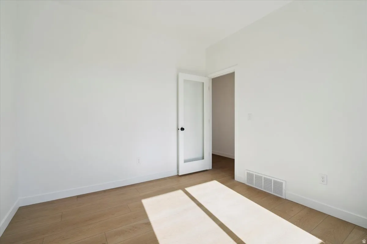 Bright interior space featuring light wood-finish flooring, white walls, and a contemporary door with a frosted glass panel and black hardware