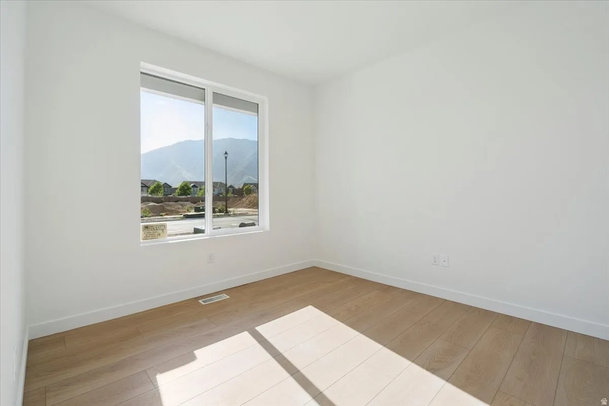 Spacious room with light wood-finish flooring, crisp white walls, and bright white baseboards