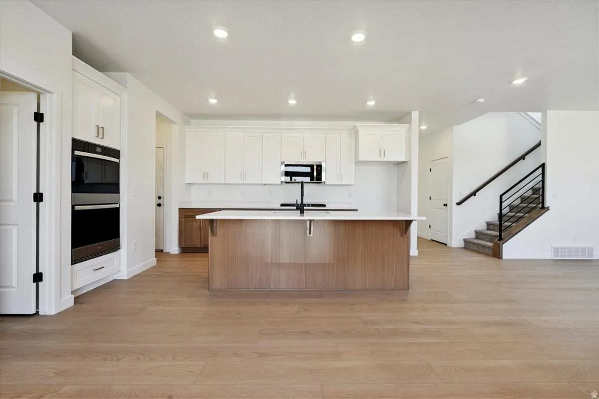 Open-concept kitchen featuring an oversized island with a white countertop, two-tone cabinetry, stainless steel double wall ovens, and wood-finish flooring