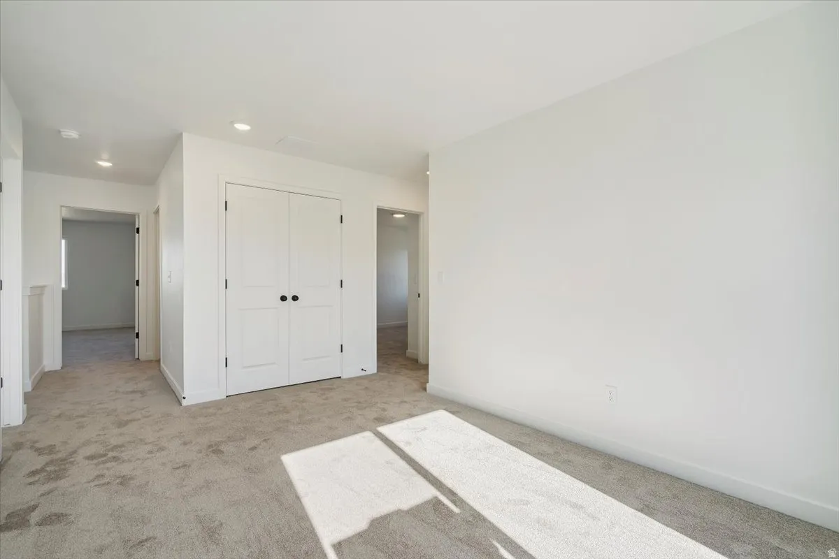 Spacious room featuring neutral carpeting, white walls, recessed ceiling lighting, and a double-door closet with matte black hardware