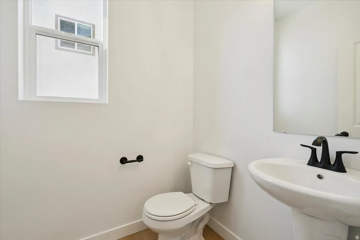 Pedestal sink with a matte black faucet, wall-mounted mirror, and white toilet