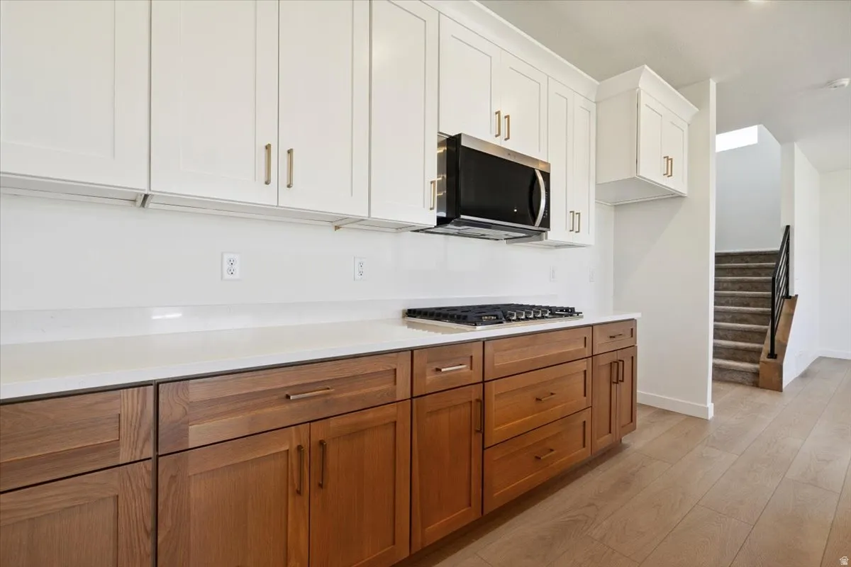 Kitchen featuring two-tone cabinetry with white upper cabinets and wood-finish lower cabinets, quartz countertops, and a gas range with an overhead microwave