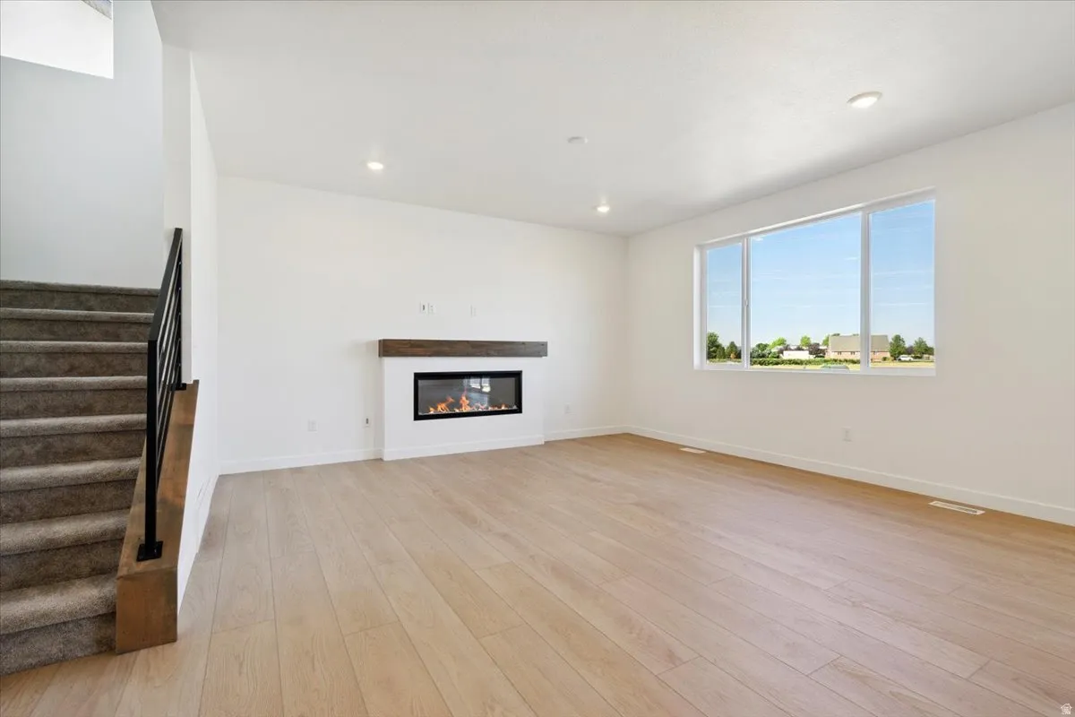 Open-concept living space featuring light wood-finish flooring, a modern linear fireplace with a wood mantle, and recessed ceiling lighting