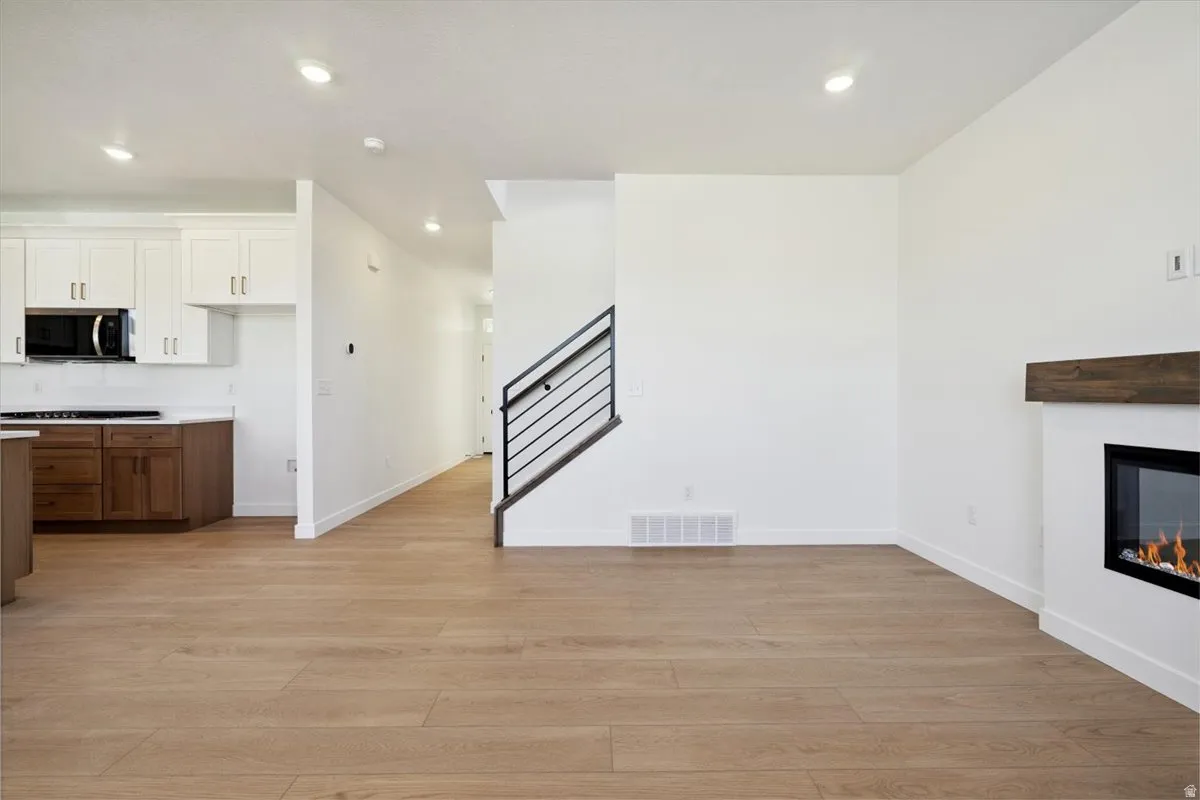 Open-concept living area featuring wood-finish flooring, recessed lighting, and a modern fireplace with a wood mantle