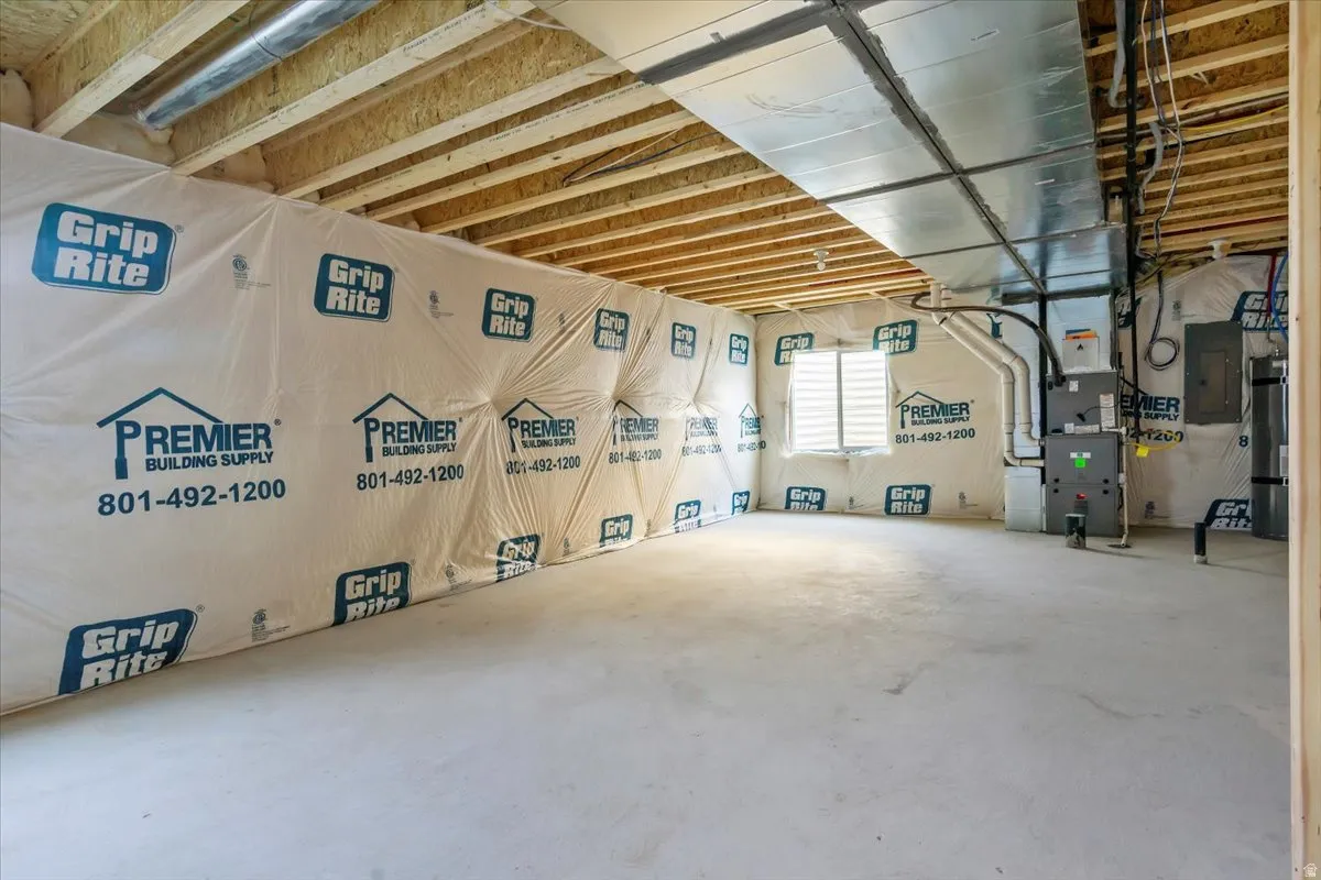 Unfinished basement featuring exposed wood joists, concrete flooring, a single window with horizontal blinds, and visible HVAC ductwork and utility connections