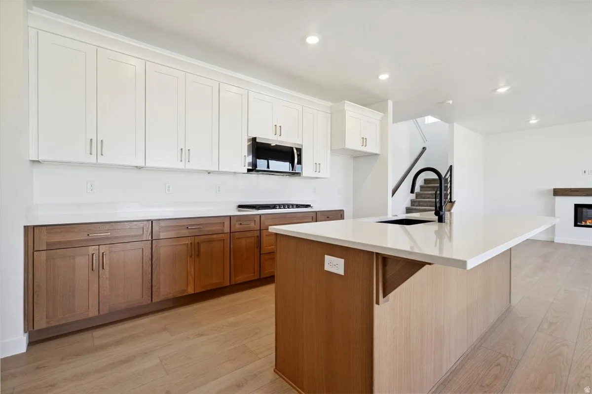 Modern kitchen featuring a large center island with a black sink and faucet, two-tone cabinetry, stainless steel appliances, and light wood-finish flooring