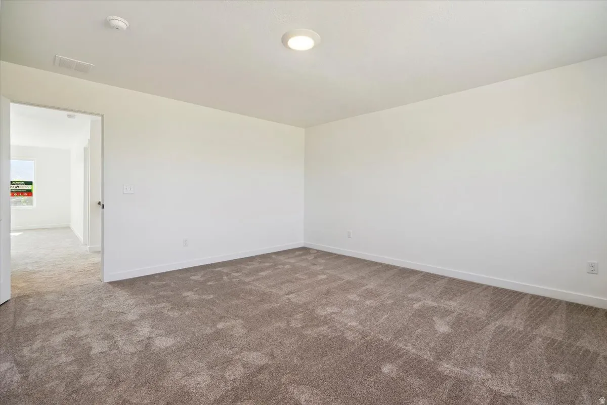 Spacious interior room featuring neutral-toned carpeting, white walls, and a flush-mount ceiling light