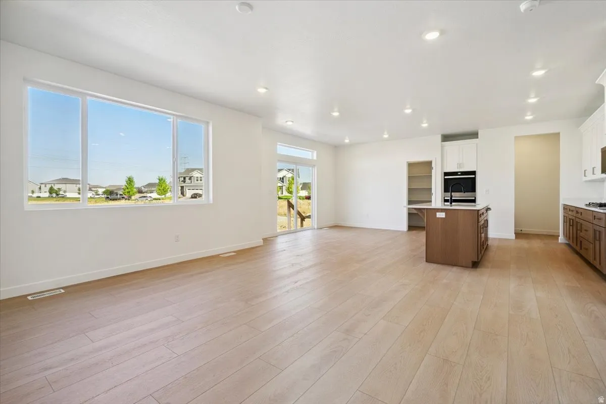 Spacious open-concept living area featuring light wood-finish flooring, recessed lighting, and a large multi-pane window