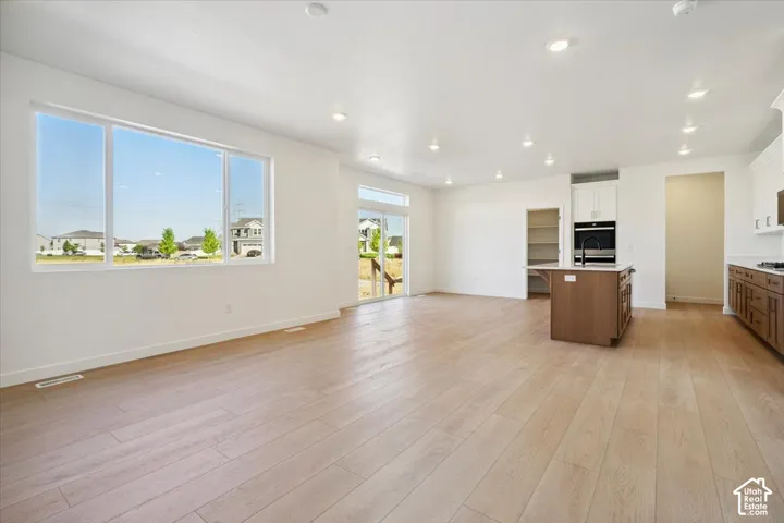 Spacious open-concept living area featuring light wood-finish flooring, recessed lighting, and a large multi-pane window