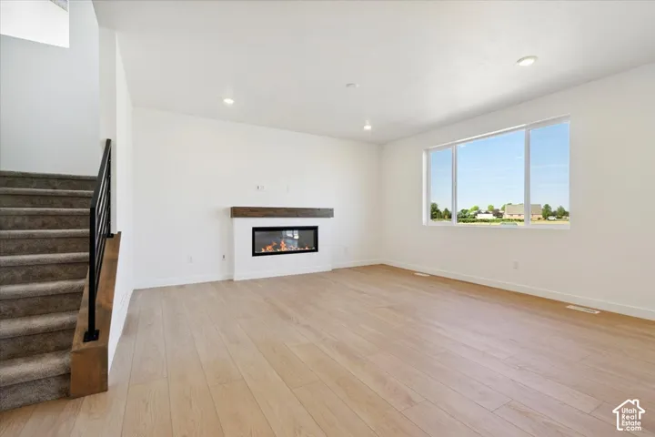 Open-concept living space featuring light wood-finish flooring, a modern linear fireplace with a wood mantle, and recessed ceiling lighting