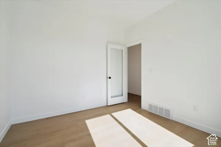 Bright interior space featuring light wood-finish flooring, white walls, and a contemporary door with a frosted glass panel and black hardware
