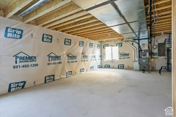 Unfinished basement featuring exposed wood joists, concrete flooring, a single window with horizontal blinds, and visible HVAC ductwork and utility connections