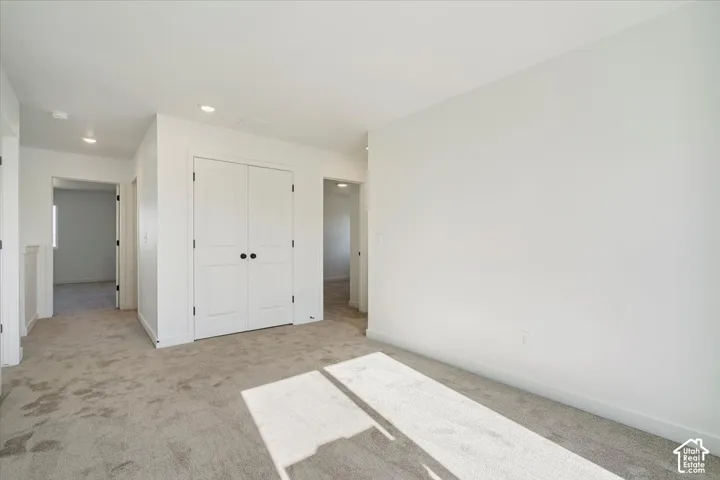 Spacious room featuring neutral carpeting, white walls, recessed ceiling lighting, and a double-door closet with matte black hardware