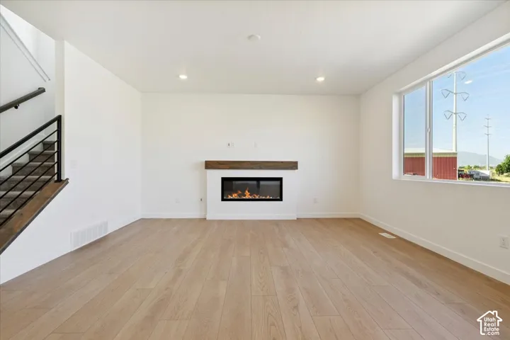Spacious living area featuring wood-finish flooring, a modern fireplace with a wood mantle, and large windows