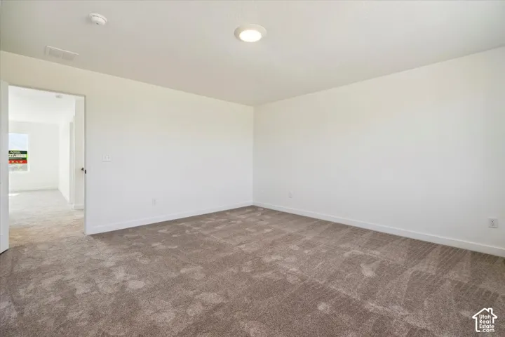 Spacious interior room featuring neutral-toned carpeting, white walls, and a flush-mount ceiling light