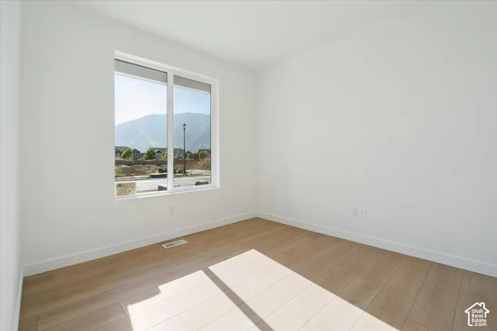 Spacious room with light wood-finish flooring, crisp white walls, and bright white baseboards