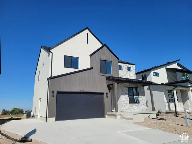 Contemporary two-story exterior with a mixed material facade, featuring a prominent dark gray garage door, a covered entryway with stone-look detailing, and a clean concrete driveway