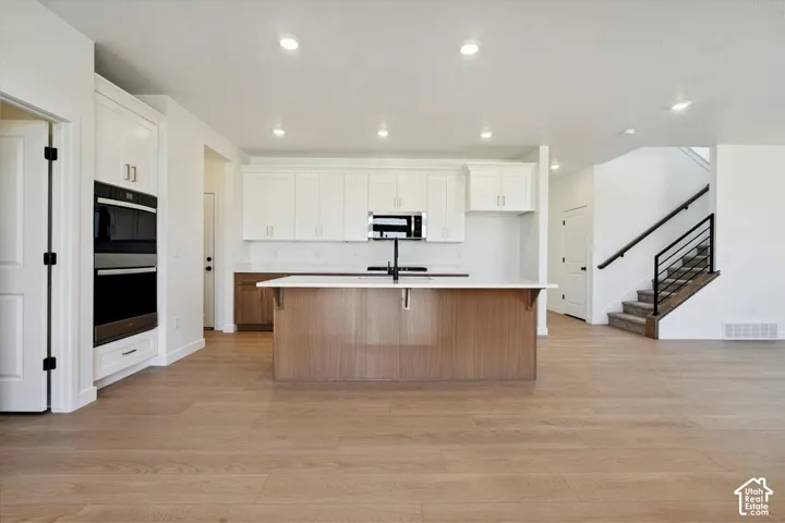Open-concept kitchen featuring an oversized island with a white countertop, two-tone cabinetry, stainless steel double wall ovens, and wood-finish flooring