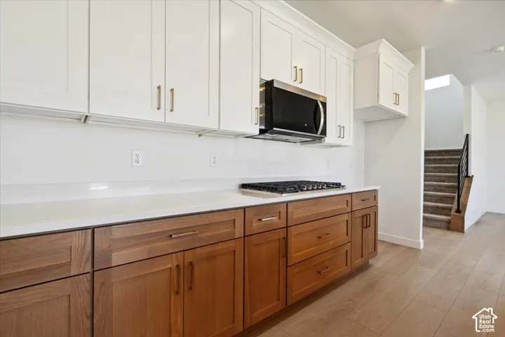 Kitchen featuring two-tone cabinetry with white upper cabinets and wood-finish lower cabinets, quartz countertops, and a gas range with an overhead microwave