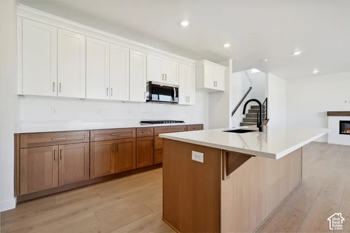 Modern kitchen featuring a large center island with a black sink and faucet, two-tone cabinetry, stainless steel appliances, and light wood-finish flooring