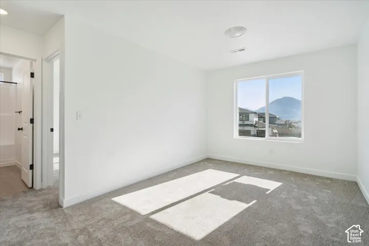 Bright room featuring a large window, soft gray carpet, white walls, and a ceiling-mounted light fixture