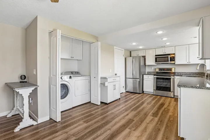 Kitchen featuring wood-finish flooring, white cabinetry, stainless steel appliances, and granite-look countertops
