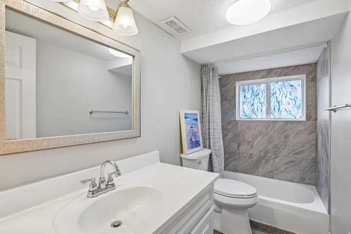 Bathroom featuring a built-in bathtub with a tiled surround, a window, a white vanity with an integrated sink, a chrome faucet, and a large framed mirror