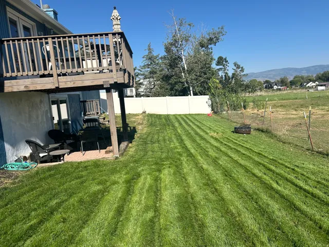 Expansive rear yard with manicured lawn, a two-story deck, a ground-level patio, and a privacy fence