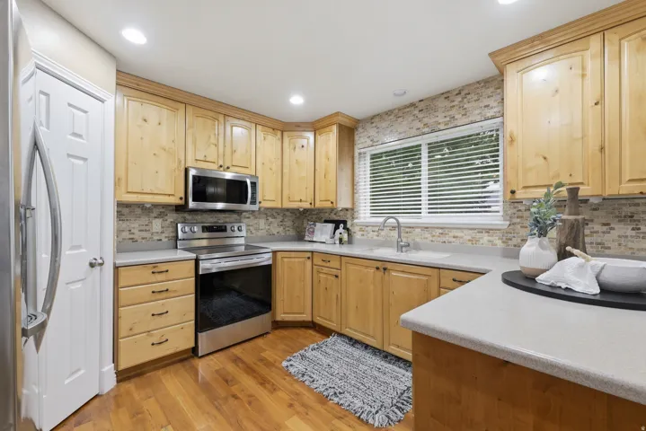 Kitchen featuring wood-finish cabinetry, stainless steel appliances, light countertops, and a mosaic tile backsplash