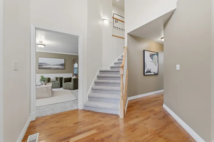 Foyer featuring wood-finish flooring, a carpeted staircase with wood banister, and a wall sconce