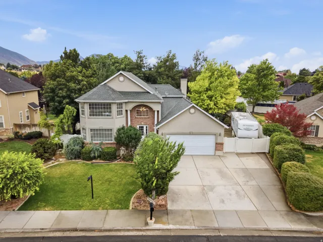 Stucco and brick exterior with a multi-gabled roof, featuring a two-car garage, mature landscaping, and an extended concrete driveway